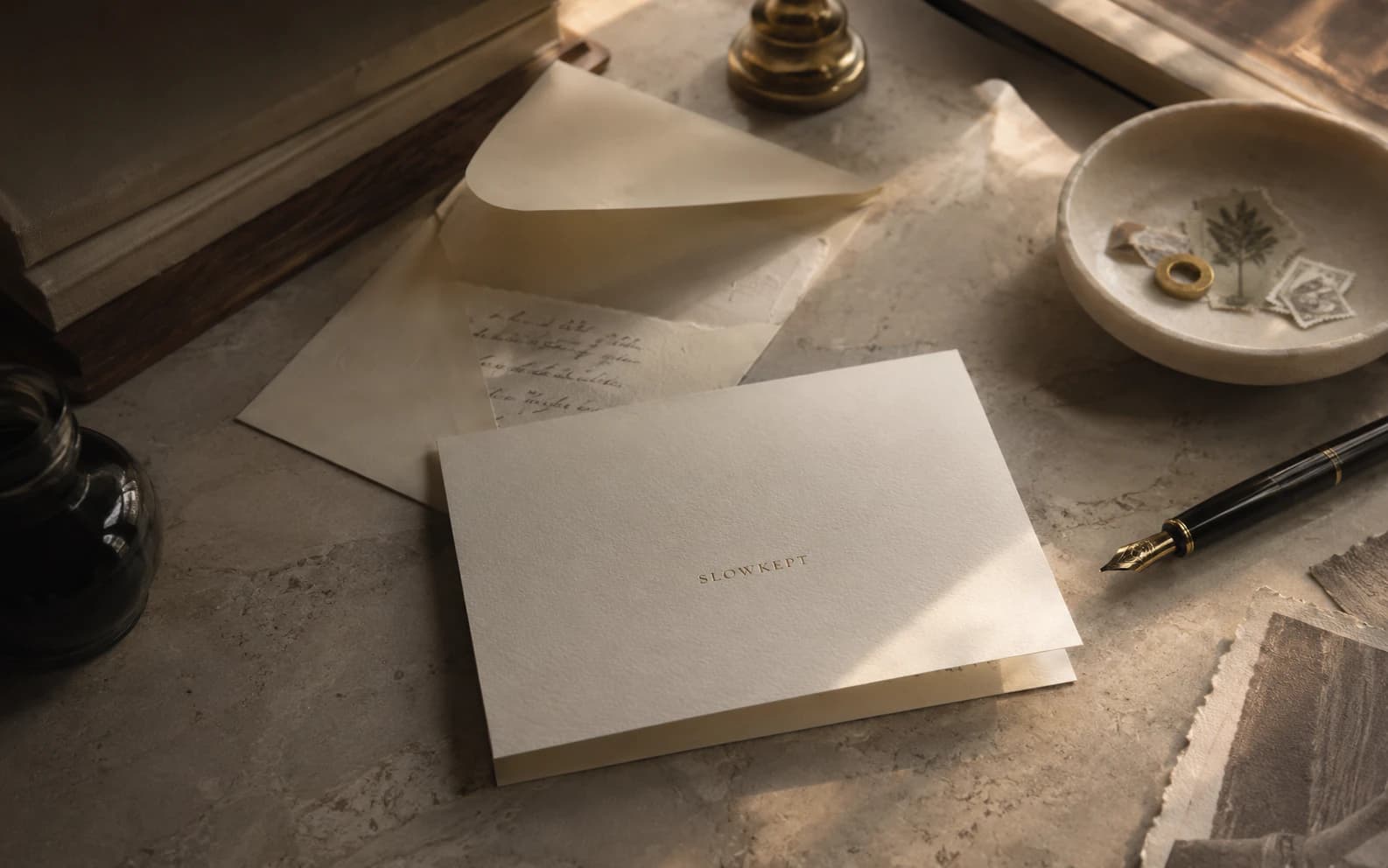 A SLOWKEPT still life with letter paper, an envelope, an ink bottle, and warm light